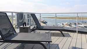 A balcony with two lounge chairs, a small table, and a view of a marina with boats. - 5 Star Holiday Home in Wendtorf (Lubeck)