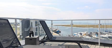 A balcony with two lounge chairs, a small table, and a view of a marina with boats.