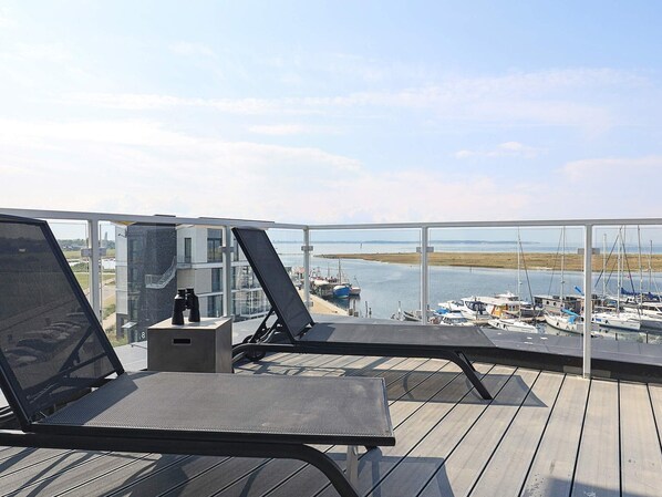 Un balcon avec deux fauteuils de jardin, une petite table et une vue sur une marina remplie de bateaux.