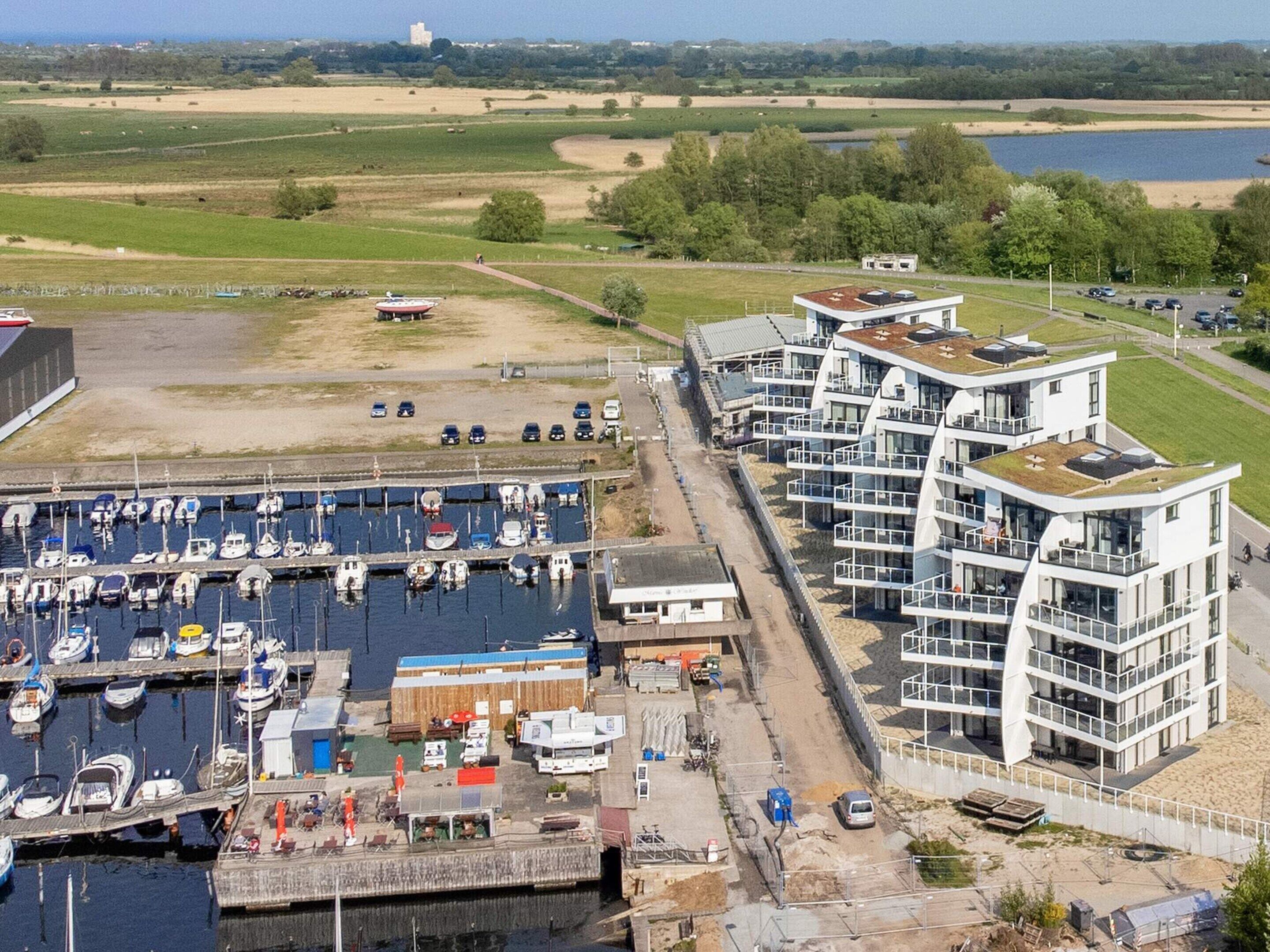 Uma marina com barcos, um edifício moderno com varandas e vista para a paisagem circundante.