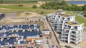 Uma marina com barcos, um edifício moderno com varandas e vista para a paisagem circundante.