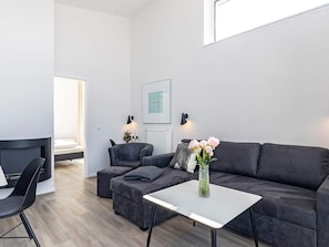 Uma sala de estar moderna com sofá, poltrona, banquinho, uma mesinha e um vaso com flores.