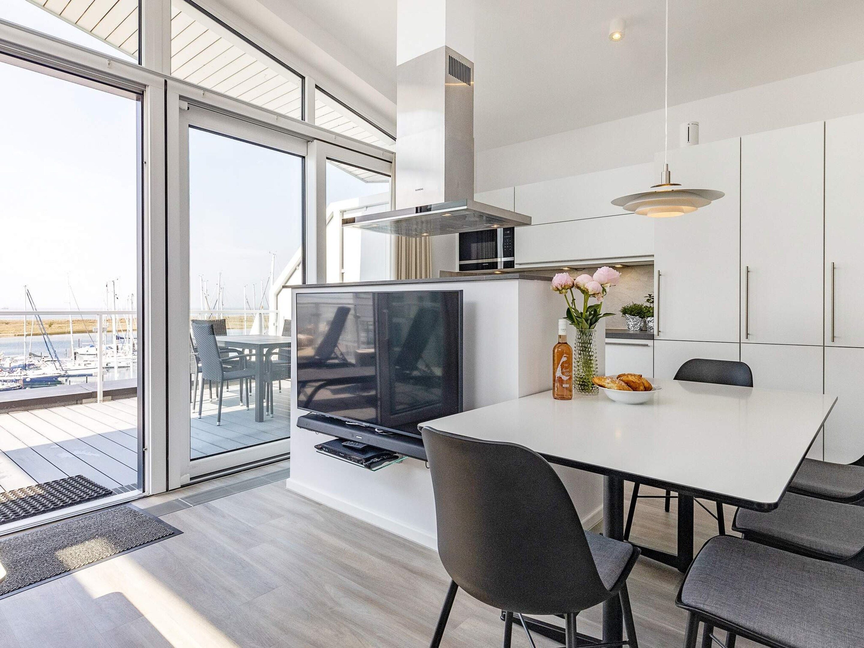 Eine moderne Küche mit einer großen Kochinsel, einem Essbereich mit Stühlen und Blick auf die Marina durch große Fenster.
