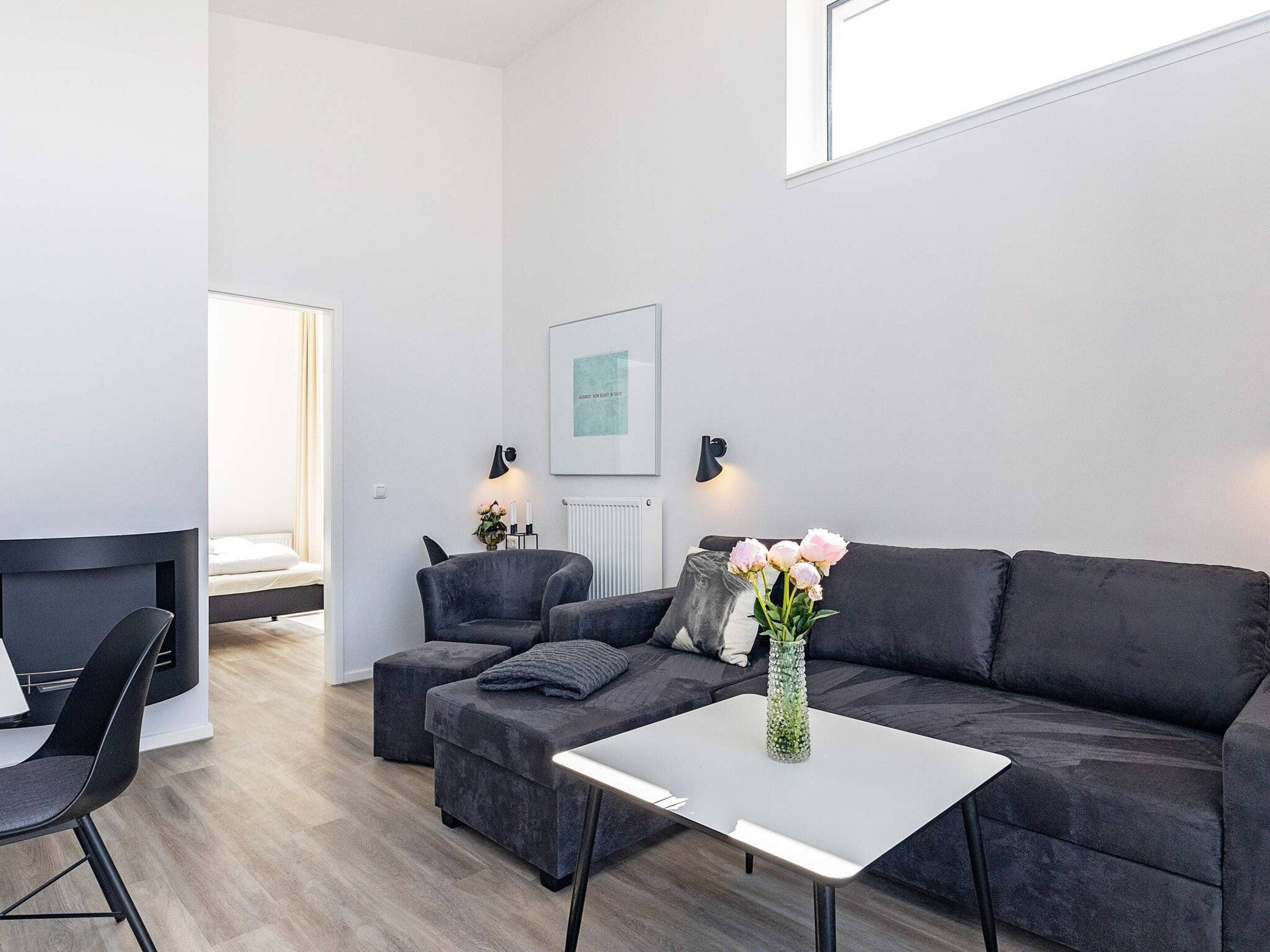 Ein modernes Wohnzimmer mit einer Couch, einem Sessel, einem Hocker, einem kleinen Tisch und einer Vase mit Blumen.