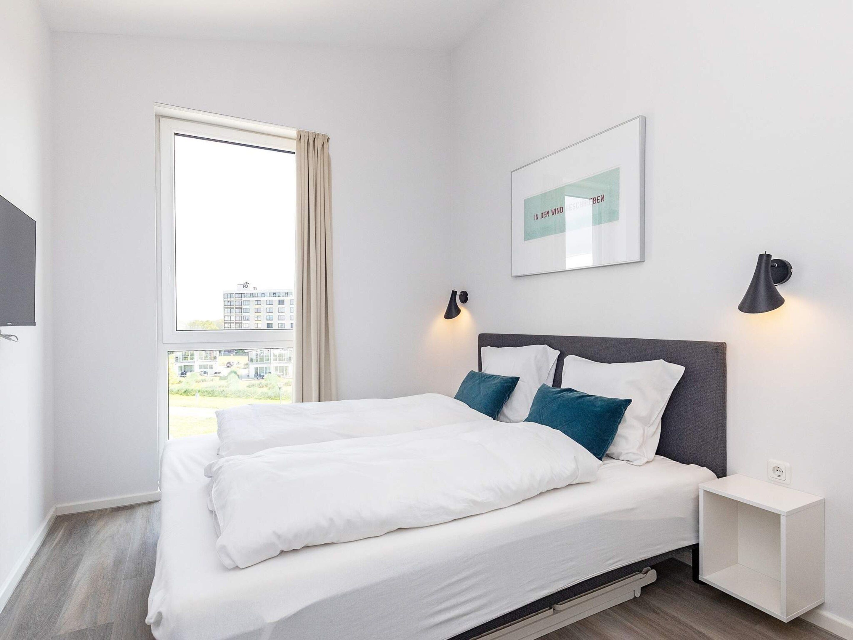 A hotel room with a bed, a nightstand, a wall-mounted lamp, and a window with curtains.