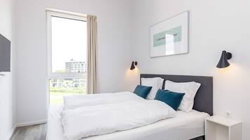 Ein Hotelzimmer mit Bett, Nachttisch, Wandlampe und einem Fenster mit Vorhängen.