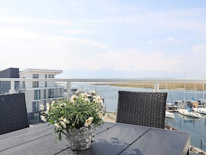 A balcony with a table and chairs, overlooking a marina with boats and a bridge in the background. - 5 Star Holiday Home in Wendtorf (Lubeck)