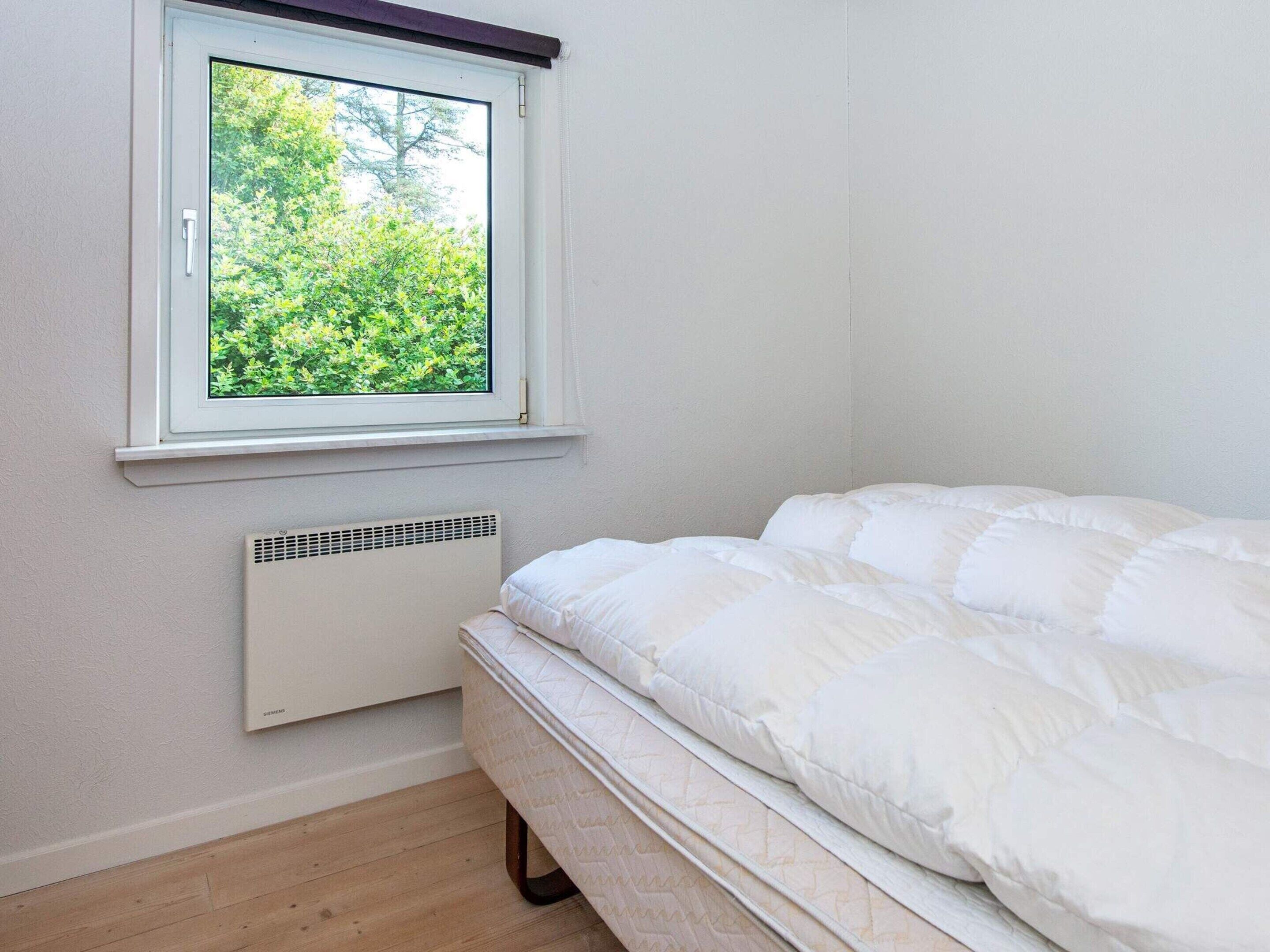 Un dormitorio con cama, ventana con vista a follaje y un calentador de pared.