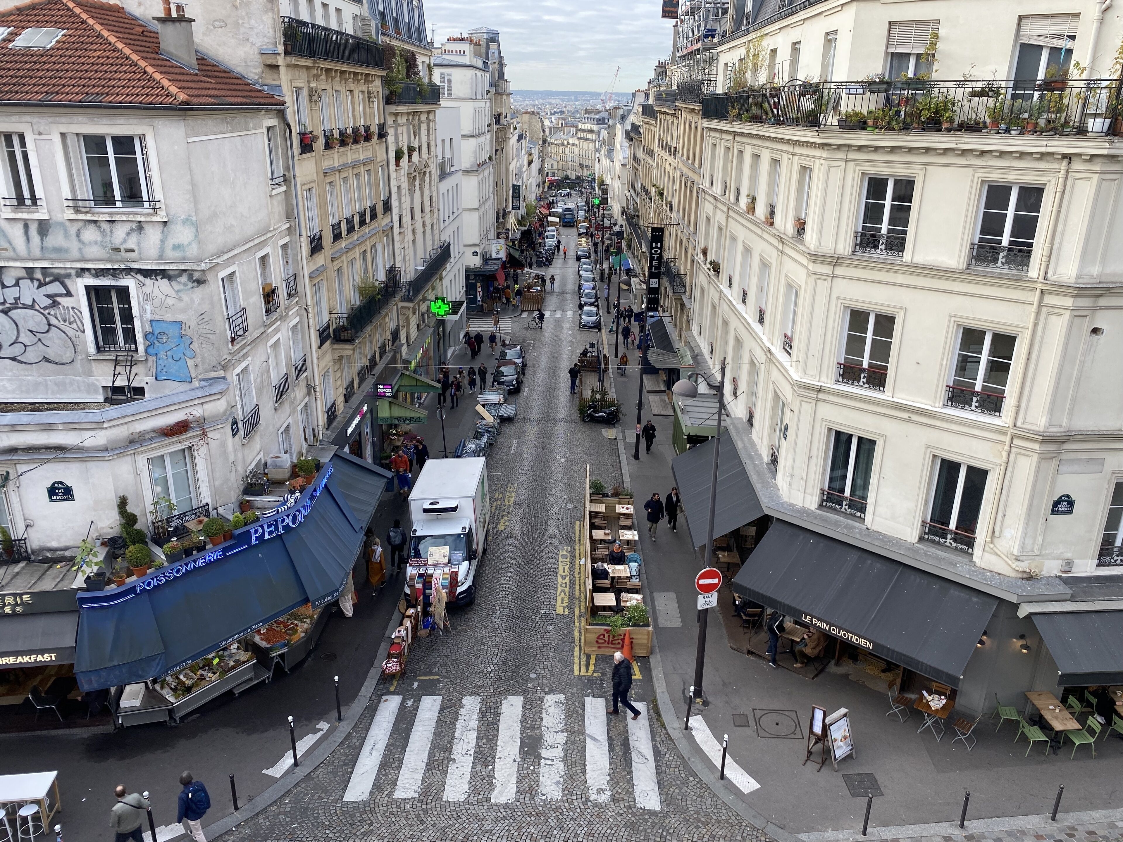 Une vue de rue avec un hôtel appelé « HOTEL » sur la droite, une zone de marché avec des étals sur la gauche et un passage piéton au centre.