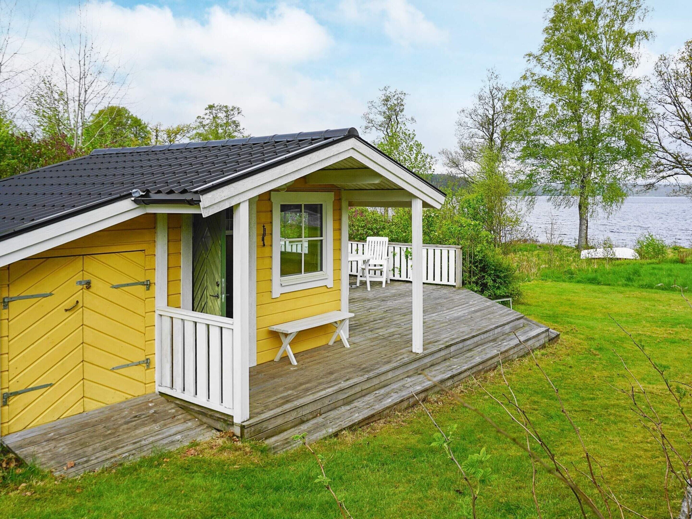 Une cabane jaune avec une terrasse en bois, un porche couvert et une vue sur un lac.