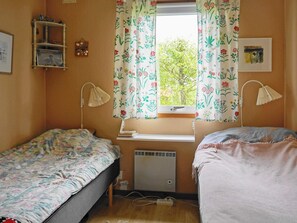 A bedroom with two beds, a window with floral curtains, a desk with a lamp, and a radiator. - 6 Person Holiday Home in Holsljunga (Holsljunga)