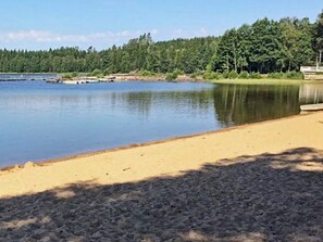 A calm lake with a sandy shore and a forest in the background. - 6 Person Holiday Home in Holsljunga (Holsljunga)