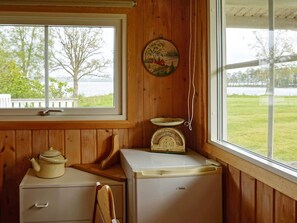 A kitchen with a wooden interior, a window with a view of a lake, a vintage scale, and a white refrigerator. - 6 Person Holiday Home in Holsljunga (Holsljunga)