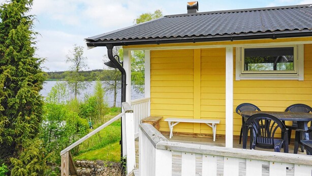 A yellow building with a porch, a table, and chairs. - 6 Person Holiday Home in Holsljunga (Holsljunga)
