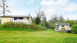 A two-story house with a porch and a small shed in a grassy yard. - 6 Person Holiday Home in Holsljunga (Holsljunga)