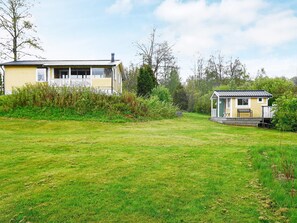 A two-story house with a porch and a small shed in a grassy yard. - 6 Person Holiday Home in Holsljunga (Holsljunga)
