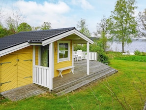 A yellow cabin with a wooden deck, a covered porch, and a view of a lake. - 6 Person Holiday Home in Holsljunga (Holsljunga)