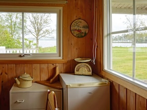 A kitchen with a stove, a refrigerator, a wooden chair, and a window with a view of a lake.