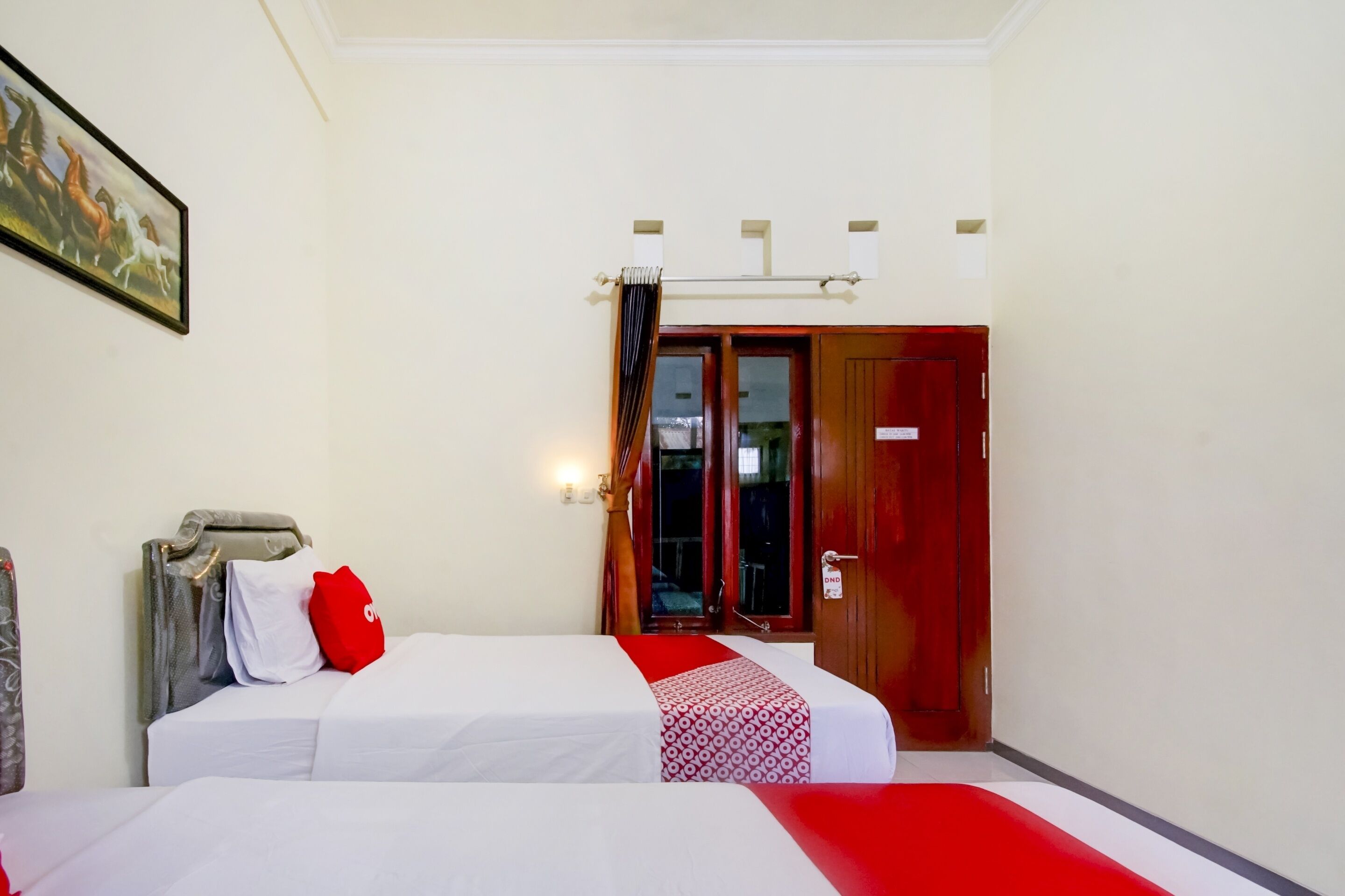 Habitación de hotel con dos camas, una puerta de madera y un cuadro en la pared.