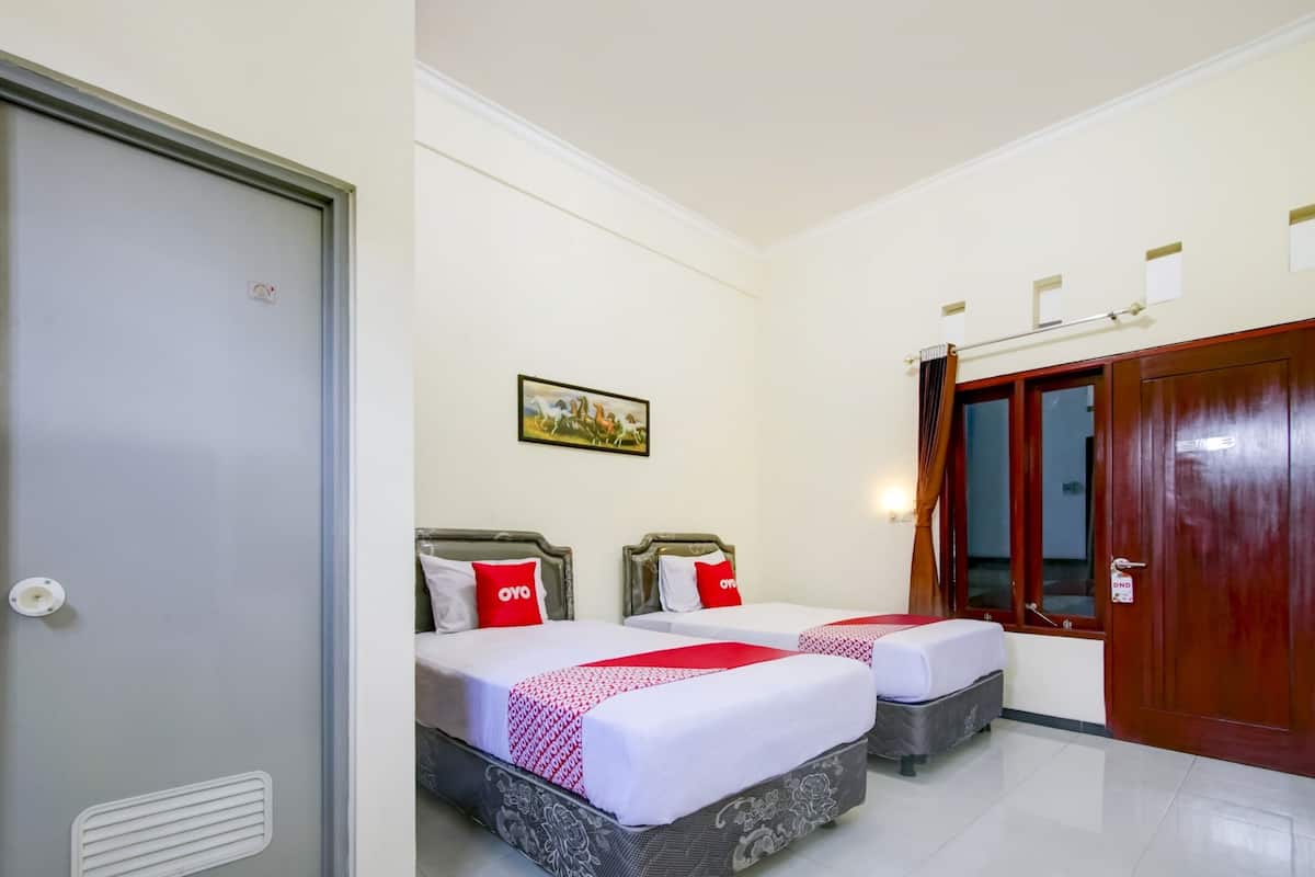 A hotel room with two beds, a wooden door, a painting on the wall, and a window with curtains.