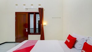 Quarto de hotel com cama, porta de madeira, janela com cortinas e luminária fixada na parede.