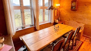 A wooden cabin with a dining table and chairs, a window with curtains, a wall-mounted clock, and a lamp. - 8 Person Holiday Home in Akra-by Traum (Kvinnherad)