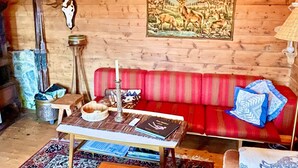A cozy log cabin interior with a red sofa, a table with books and a candle, a deer skull on the wall, and a painting of deer. - 8 Person Holiday Home in Akra-by Traum (Kvinnherad)