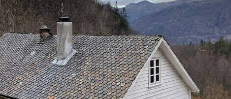 A white house with a stone roof, a chimney, and a view of mountains.