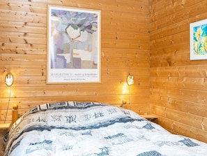 Een houten kamer met een bed, twee wandlampen en twee kunstwerken in lijsten.