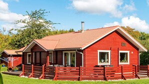 Ein rotes Holzhaus mit Ziegeldach, Schornstein und einem umzäunten Wintergarten mit Sitzgelegenheit.