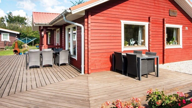 Ein rotes Holzhaus mit einer Terrasse, Gartenmöbeln und einem Fenster mit Aussicht.