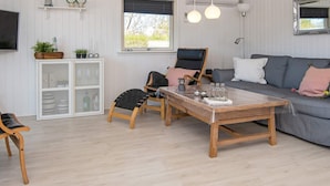 A cozy living room with a wooden coffee table, a grey sofa, and a black chair. There is a white cabinet with glass doors and a television mounted on the wall. - 4 Person Holiday Home in Hemmet (Hemmet)