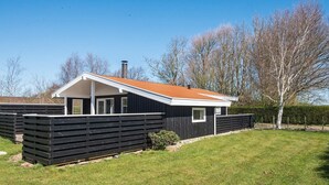 A modern house with a black exterior, a red roof, and a chimney. It is surrounded by a black fence and a grassy yard. - 4 Person Holiday Home in Hemmet (Hemmet)