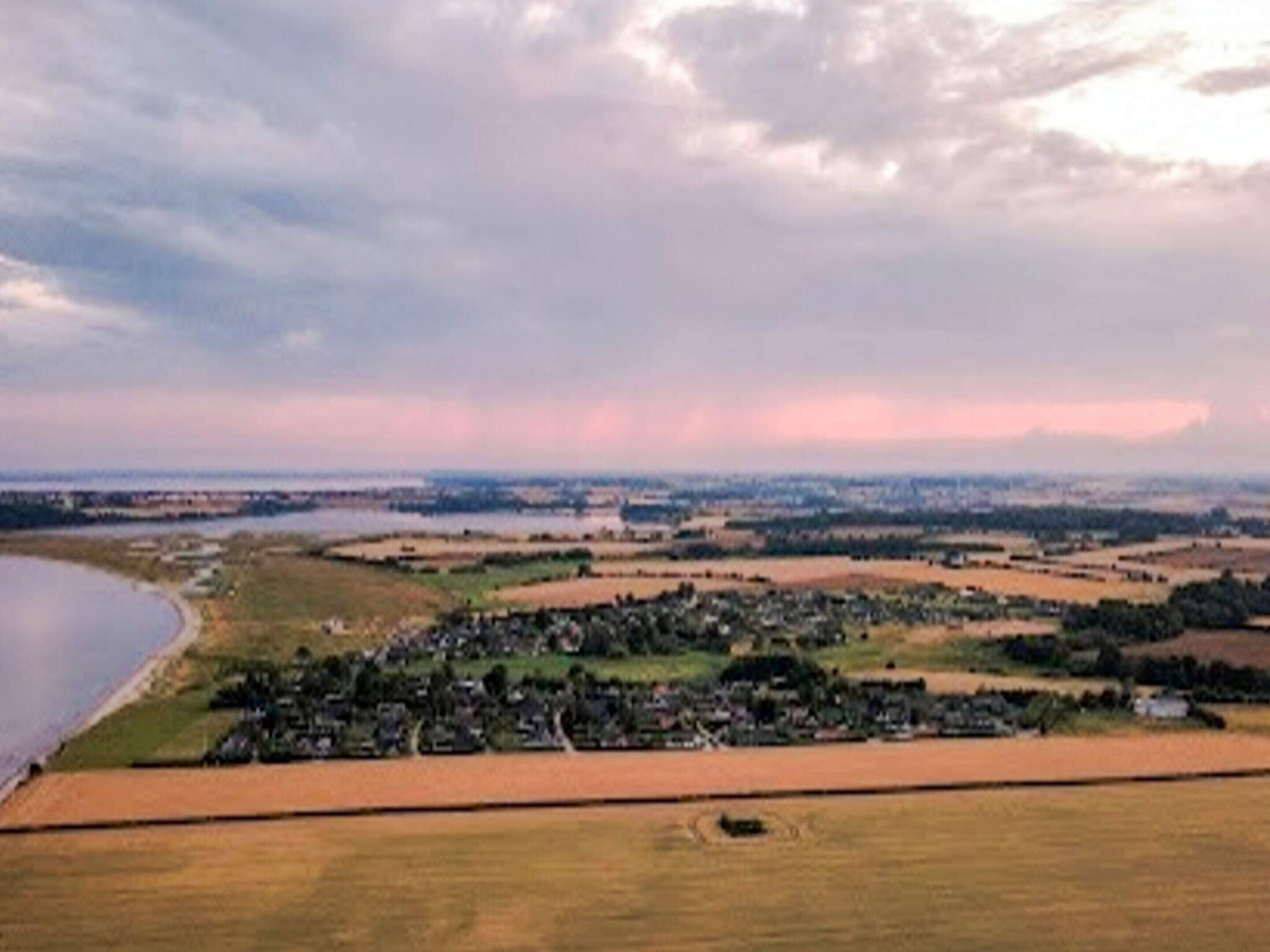 An aerial view of a rural landscape with fields, a small village, and a body of water.