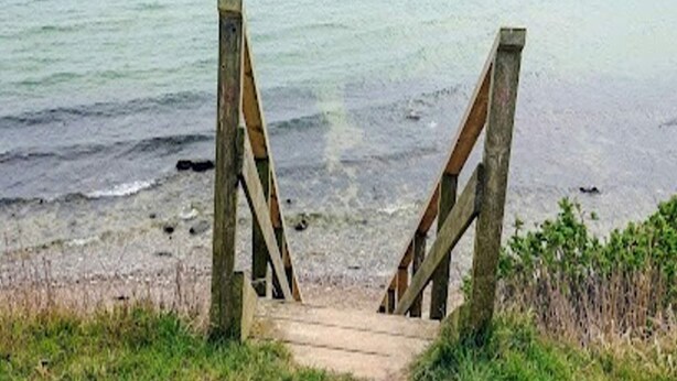 En trätrappa som leder ner till en strand med ett lugnt hav i bakgrunden.