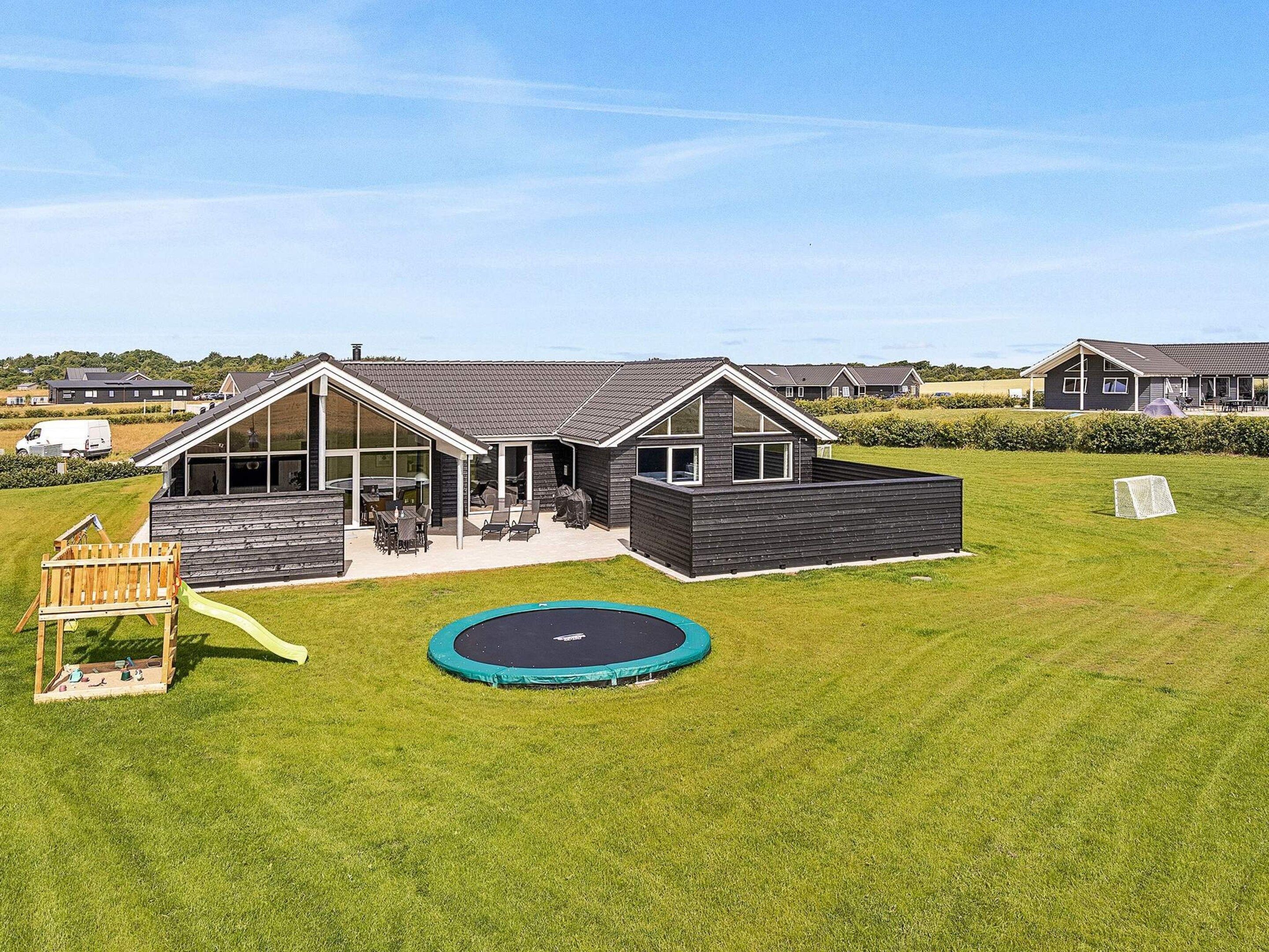 Ein modernes Haus mit Terrasse, Trampolin und Holzspielplatz.