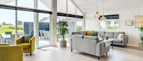 A spacious living area with a large sliding glass door leading to an outdoor patio, a grey sofa set, and a yellow armchair.