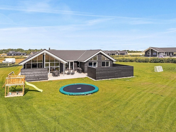 A modern house with a patio, a trampoline, and a wooden play structure.