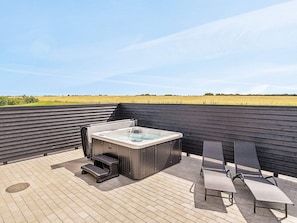 A rooftop patio with a hot tub, seating area, and a view of the countryside.