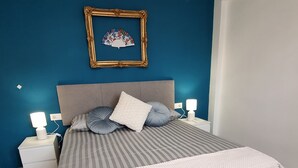 A bedroom with a bed, nightstands, a wall-mounted picture frame, and a blue accent wall. - Renovated Penthouse in the historic center, 100 meters from the Cathedral! (Almería)