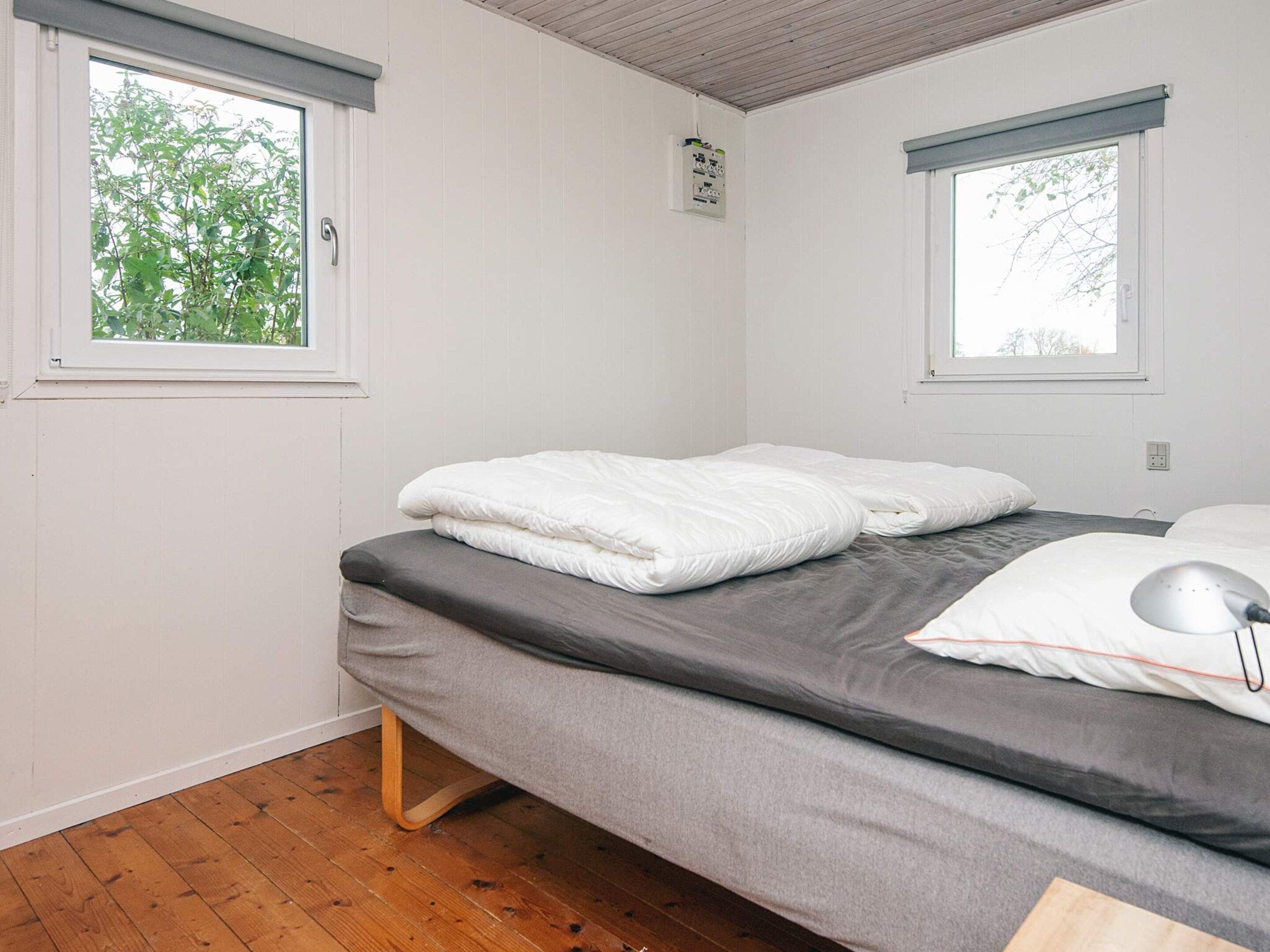 A single-bed room with a grey mattress, white pillows, and a bedside lamp.
