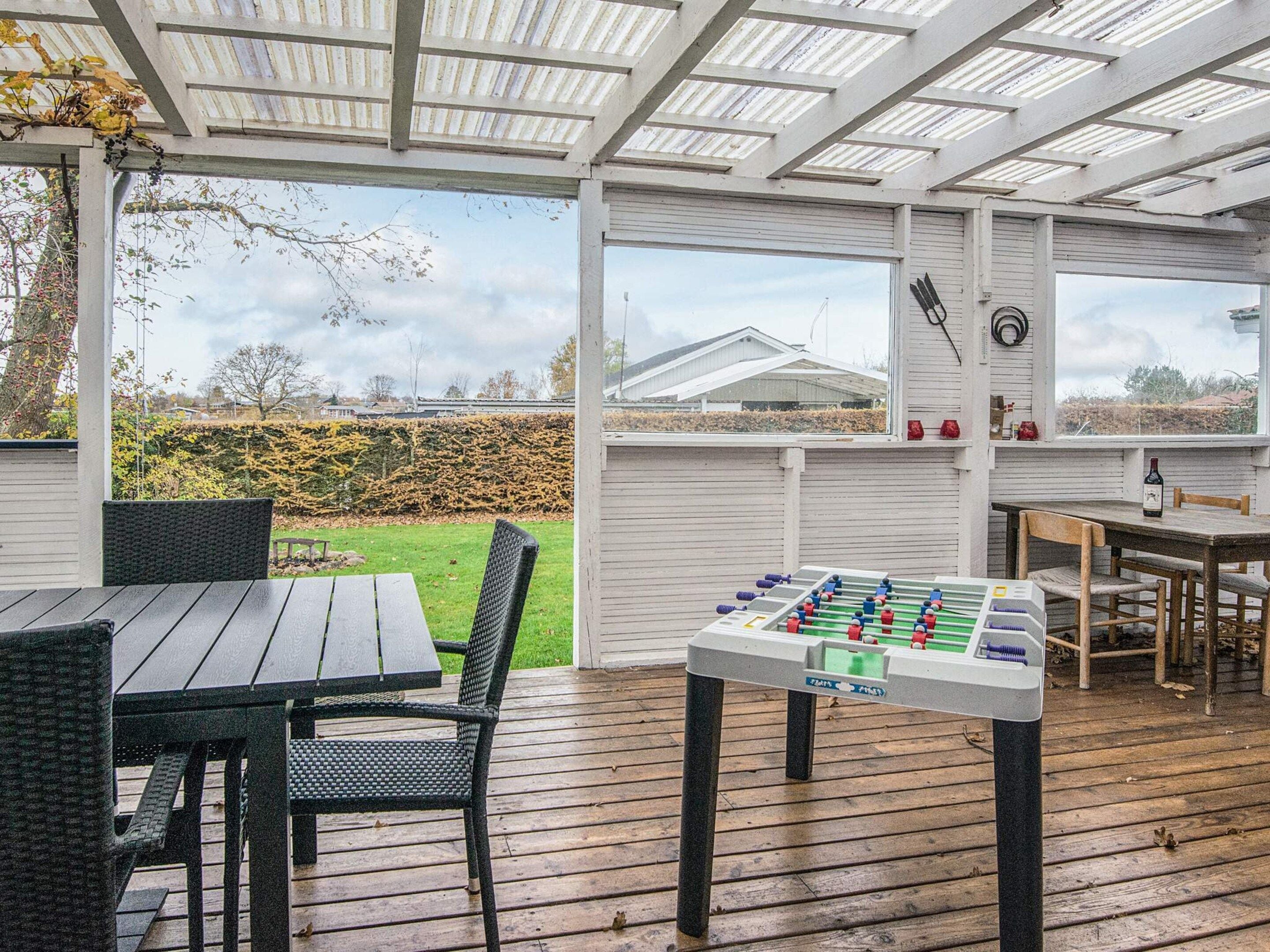 A covered outdoor area with a foosball table, a dining table, and chairs.