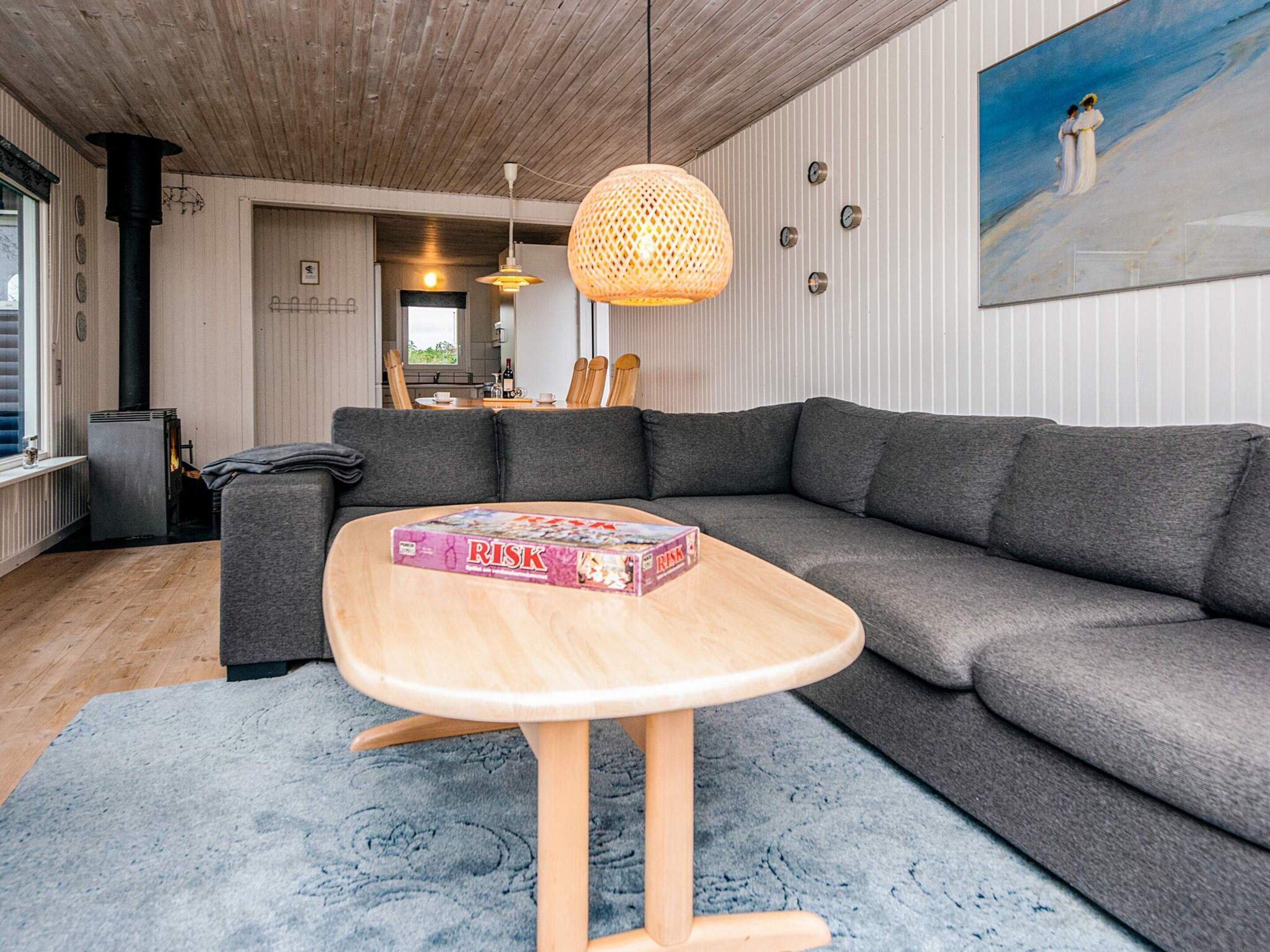 A modern living room with a grey sectional sofa, a wooden coffee table with a board game, a woven pendant light, and a painting on the wall.