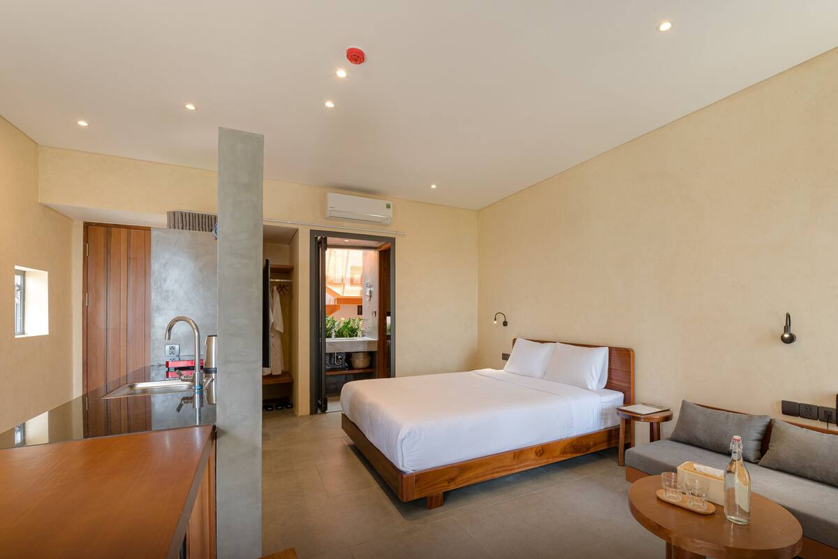 A hotel room with a bed, a sofa, a small table, a bathroom with a sink, and a shower area.