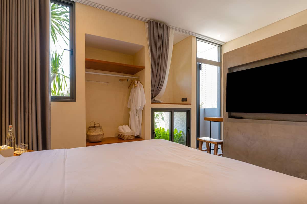 A hotel room with a large bed, a TV, a wardrobe, and a window with curtains.