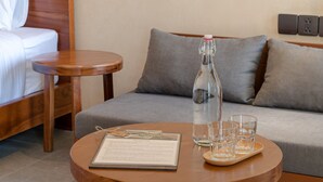A hotel room with a bed, a small wooden table with a menu, a bottle of water, and glasses. - Shelter Stay Da Nang (Da Nang)