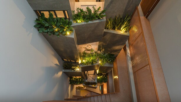 A multi-level interior with concrete pillars supporting greenery and a central staircase. - Shelter Stay Da Nang (Da Nang)