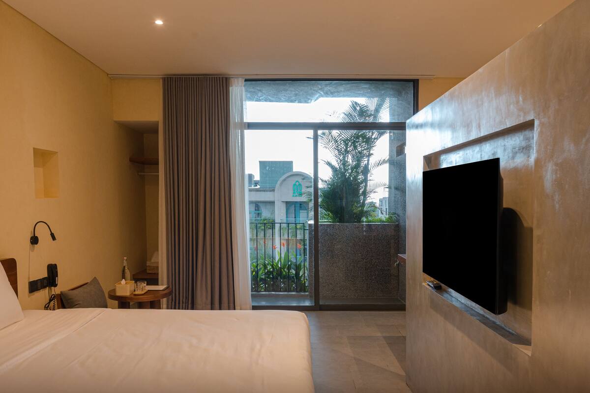 A hotel room with a bed, bedside table, lamp, and a TV mounted on the wall.