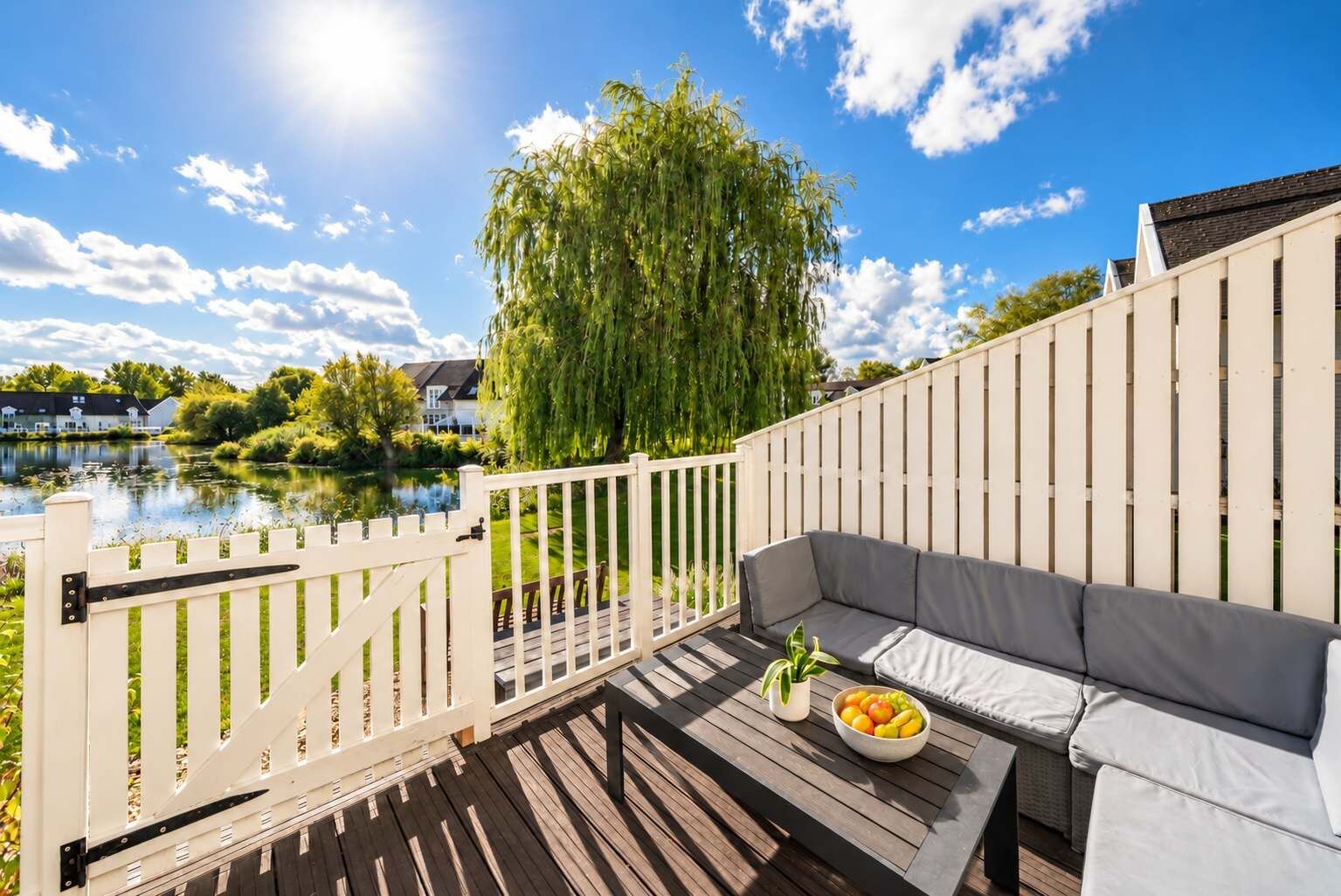 A deck with a white fence, a sofa, and a table with fruit.