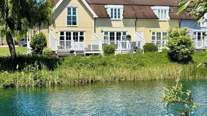 Reihenweise gelbe Häuser mit weißen Geländern an einem ruhigen Gewässer.